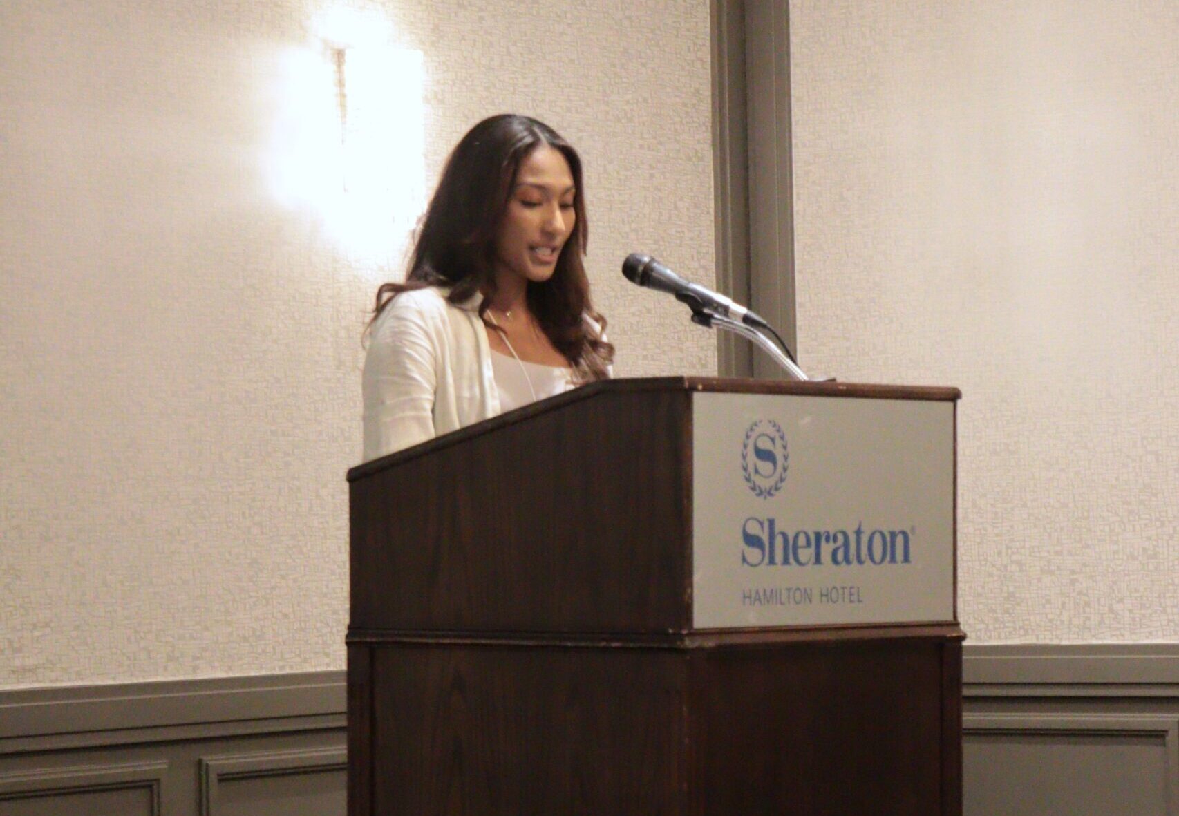 Yulika at podium speaking in a microphone at HEI Research Day